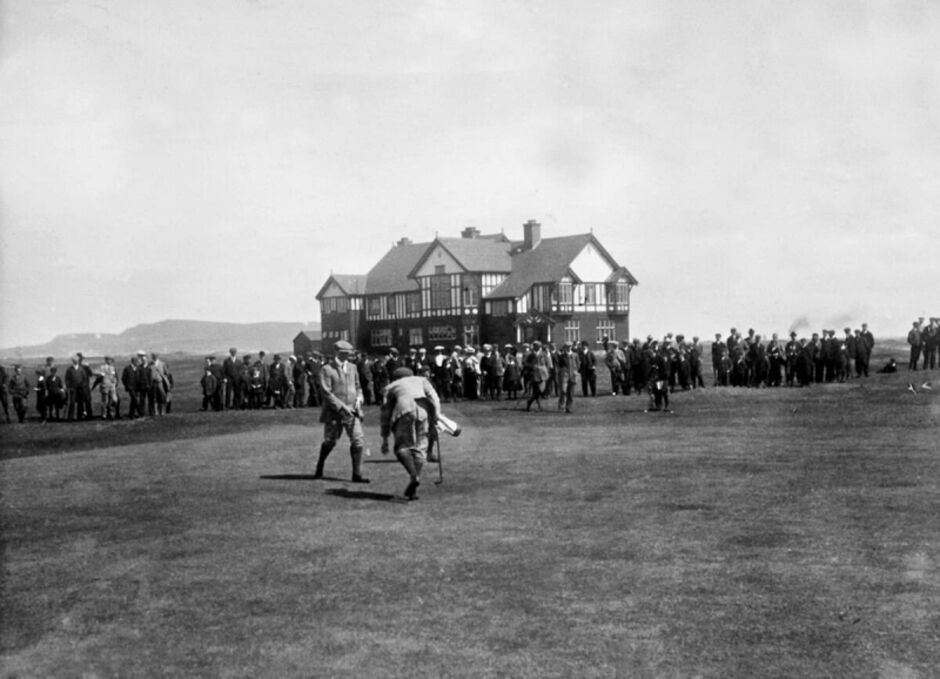 Black and white photograph of the 1905 Irish Open golf tournament, showing golfers and a caddie on the 18th green with a large crowd of spectators lining the fairway and a Tudor-style clubhouse in the background