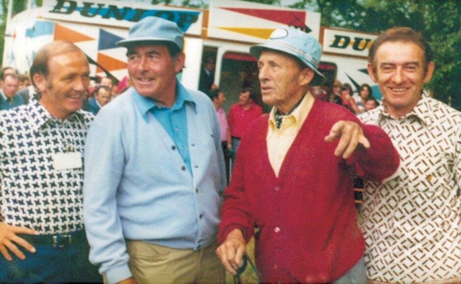 Colour photograph of Bing Crosby with three golfers at a golf tournament, posing and laughing together in front of a Dunlop branded marquee, all wearing casual 1970s leisure attire including colourful knitwear and hats