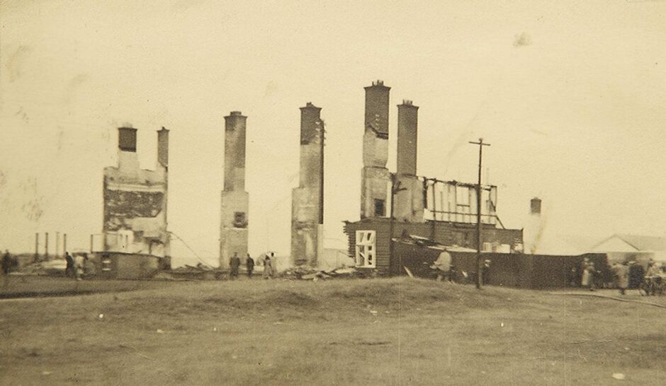 Sepia-toned historical photograph showing the burnt-out ruins of the original clubhouse at Golf Club of Dublin, with only the chimneys and partial walls remaining standing, small figures visible among the debris in the foreground