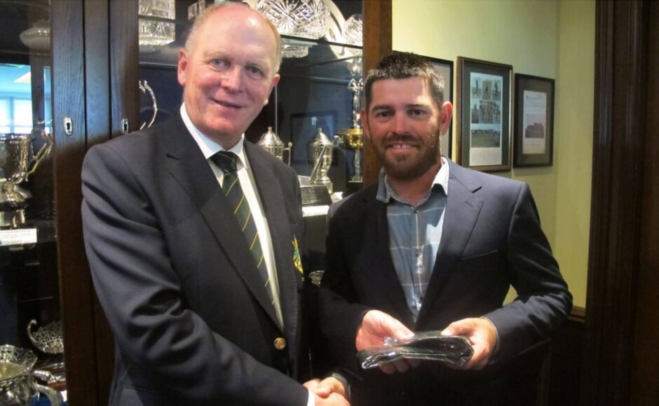 Colour photograph from June 2016 of South African golfer Louis Oosthuizen receiving a crystal glass trophy from a Golf Club of Dublin captain in a club blazer with striped tie, with a trophy cabinet visible in the background